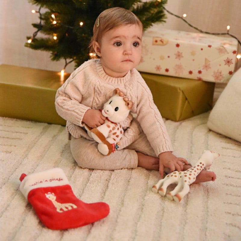 Zdjęcie poglądowe Sophie la Girafe Mon premier Noël – dziecko trzyma pluszową zabawkę przy choince